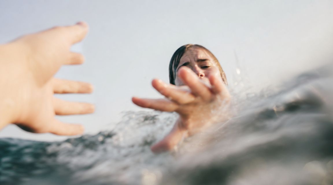 Una persona en peligro en el agua extiende su mano buscando auxilio frente a una ayuda externa.